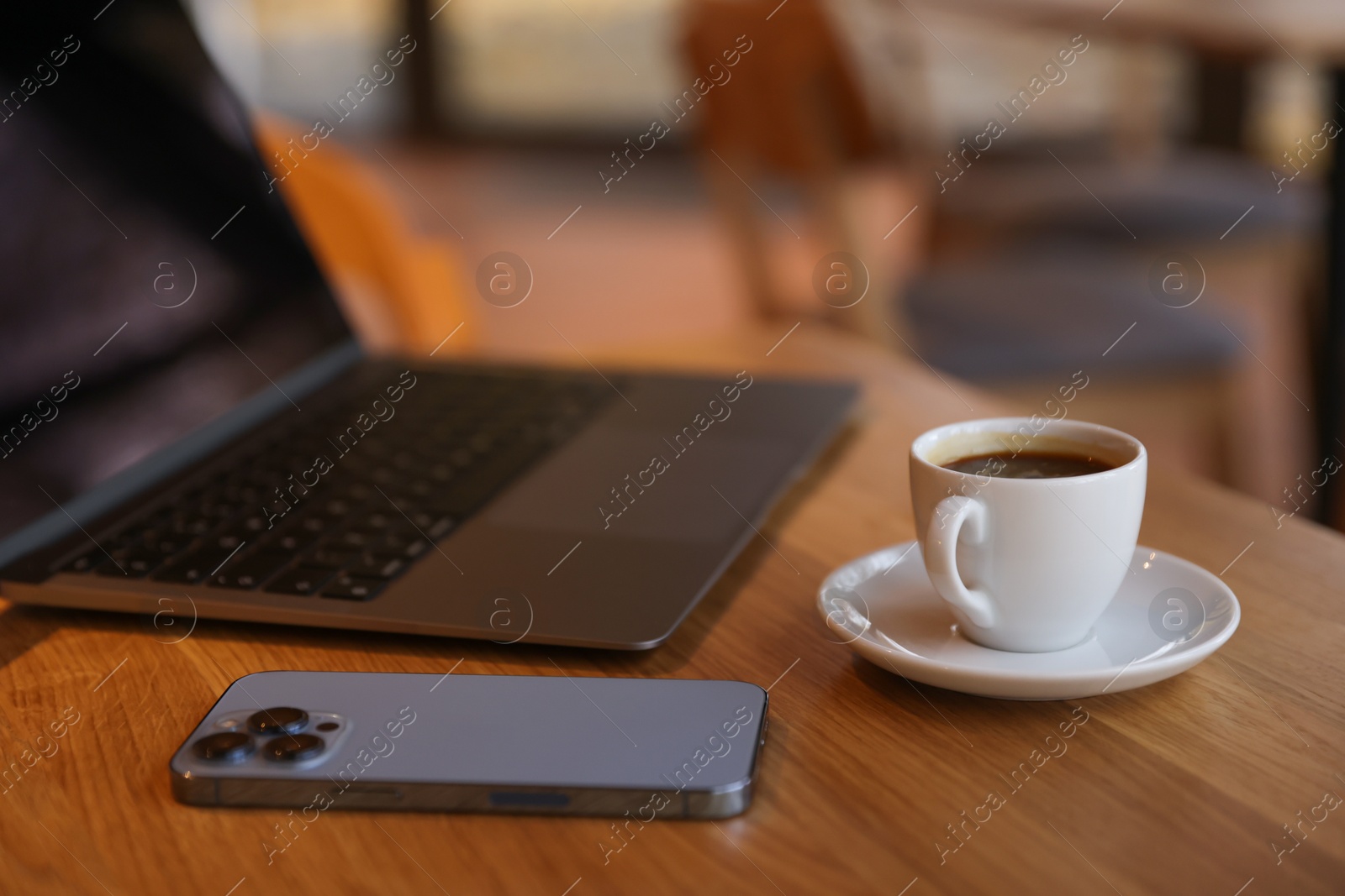 Photo of Laptop, cup of coffee and smartphone on wooden table in cafe, closeup