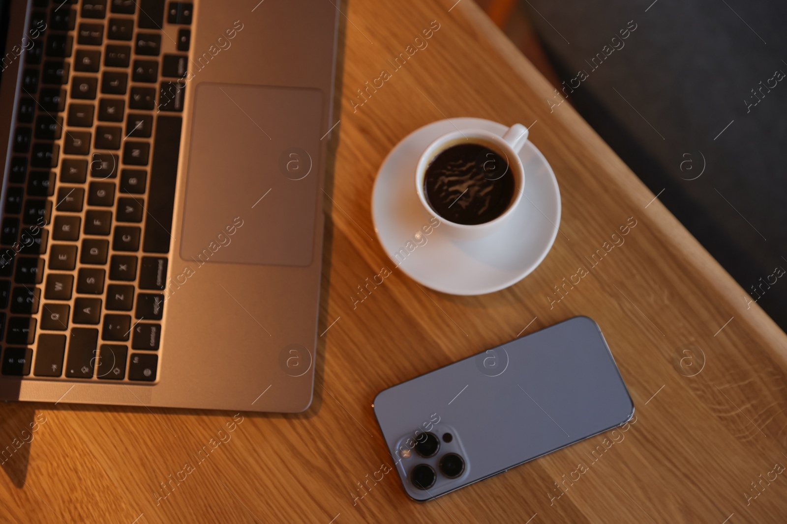 Photo of Laptop, cup of coffee and smartphone on wooden table in cafe, above view