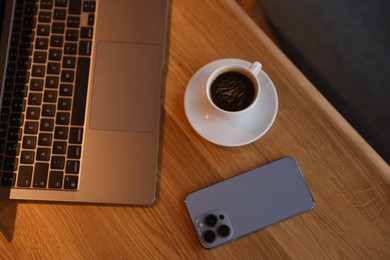 Photo of Laptop, cup of coffee and smartphone on wooden table in cafe, above view