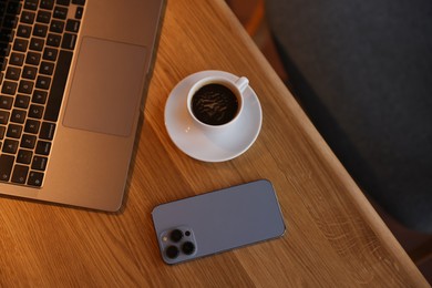 Photo of Laptop, cup of coffee and smartphone on wooden table in cafe, above view