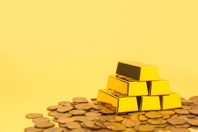 Photo of Gold bars and coins on pale yellow background, closeup. Space for text