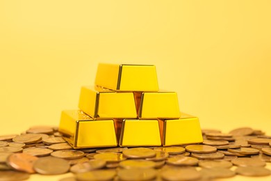 Photo of Gold bars and coins on pale yellow background, closeup