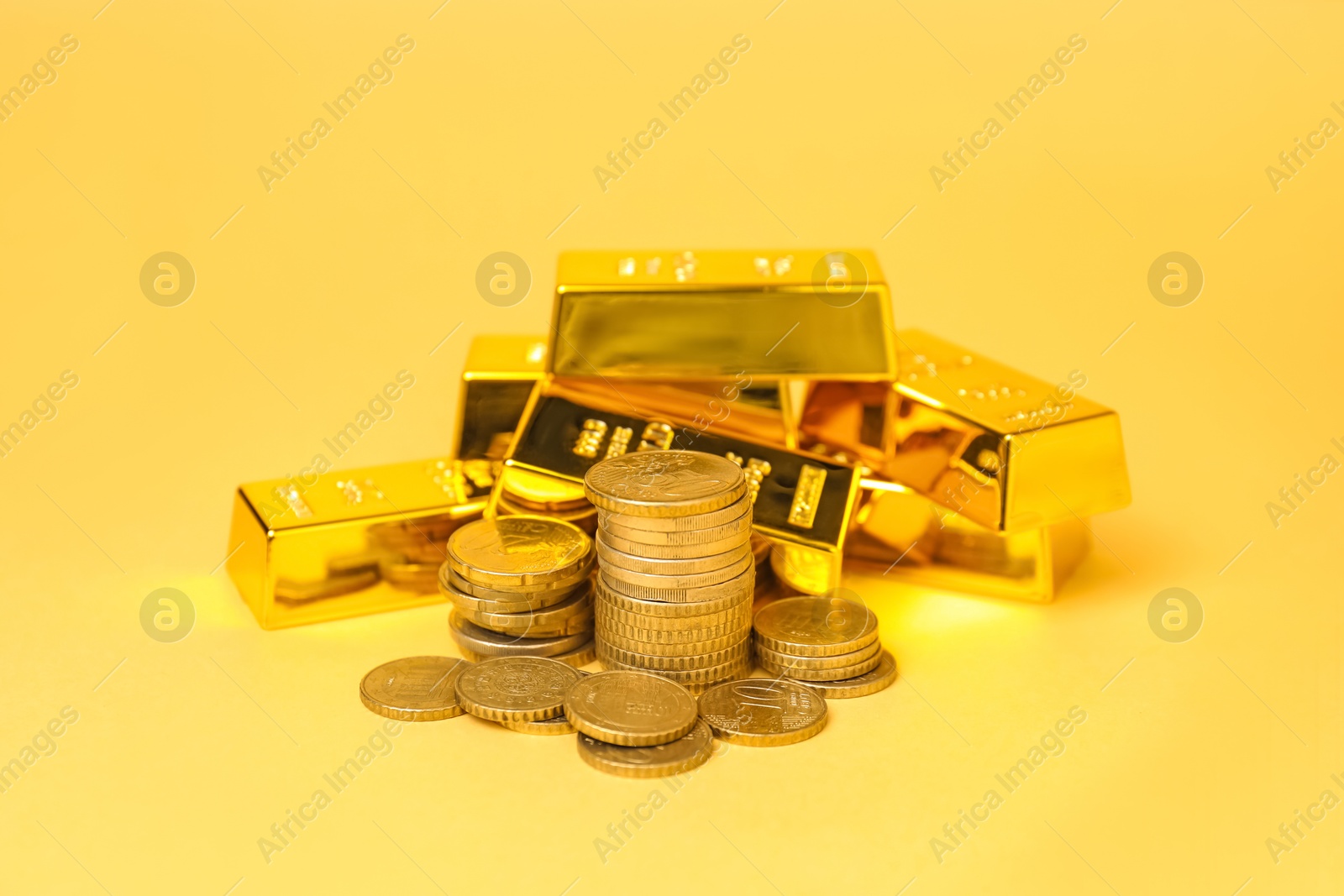 Photo of Gold bars and coins on pale yellow background, closeup