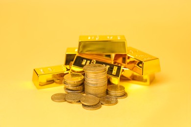 Photo of Gold bars and coins on pale yellow background, closeup