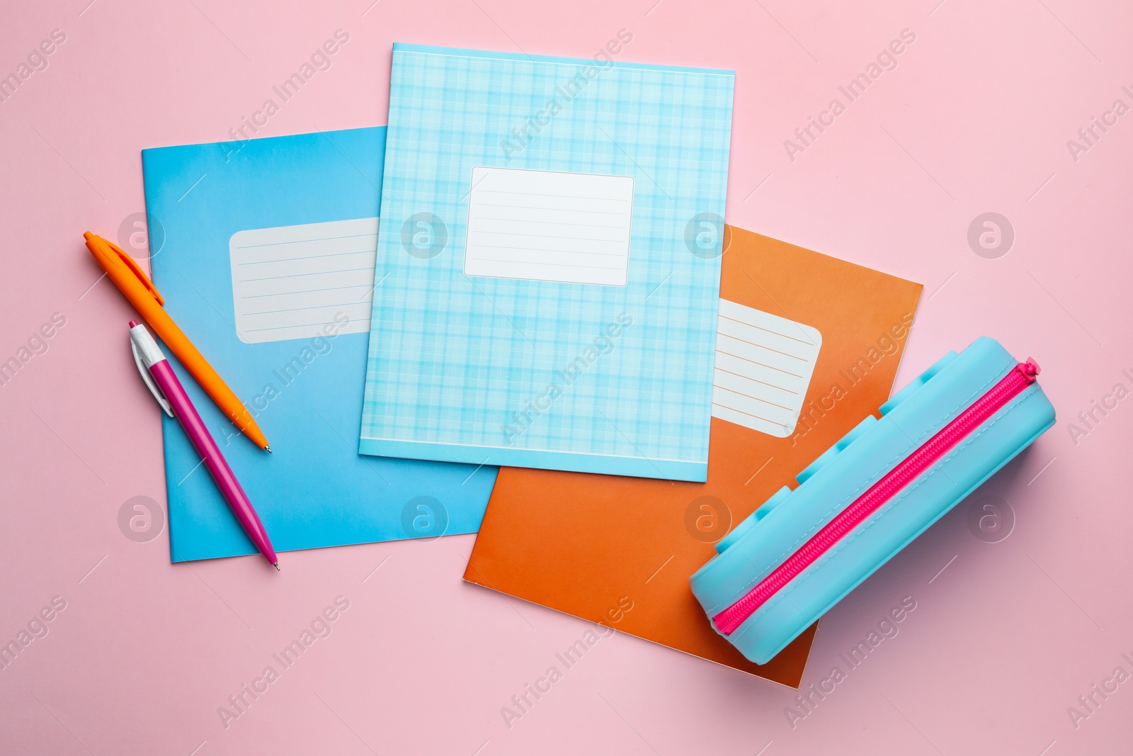 Photo of Copybooks, pens and pencil case on pink background, flat lay