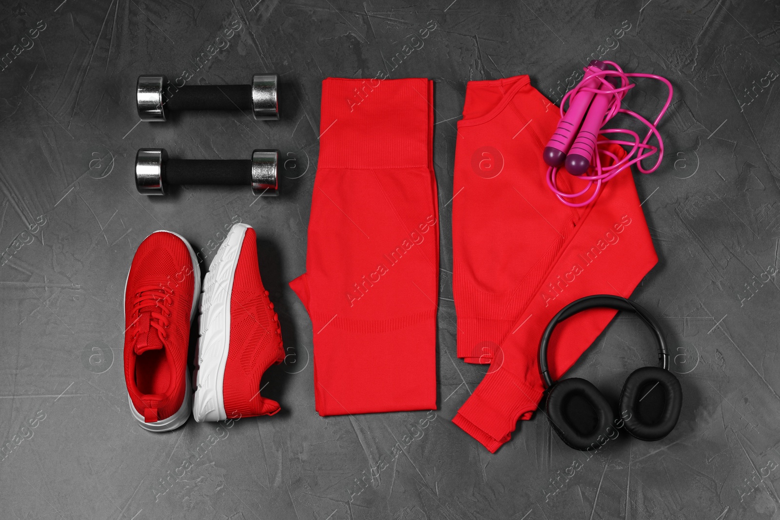 Photo of Stylish sportswear, dumbbells, red sneakers, skipping rope and headphones on grey background, flat lay