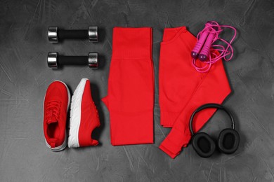 Photo of Stylish sportswear, dumbbells, red sneakers, skipping rope and headphones on grey background, flat lay