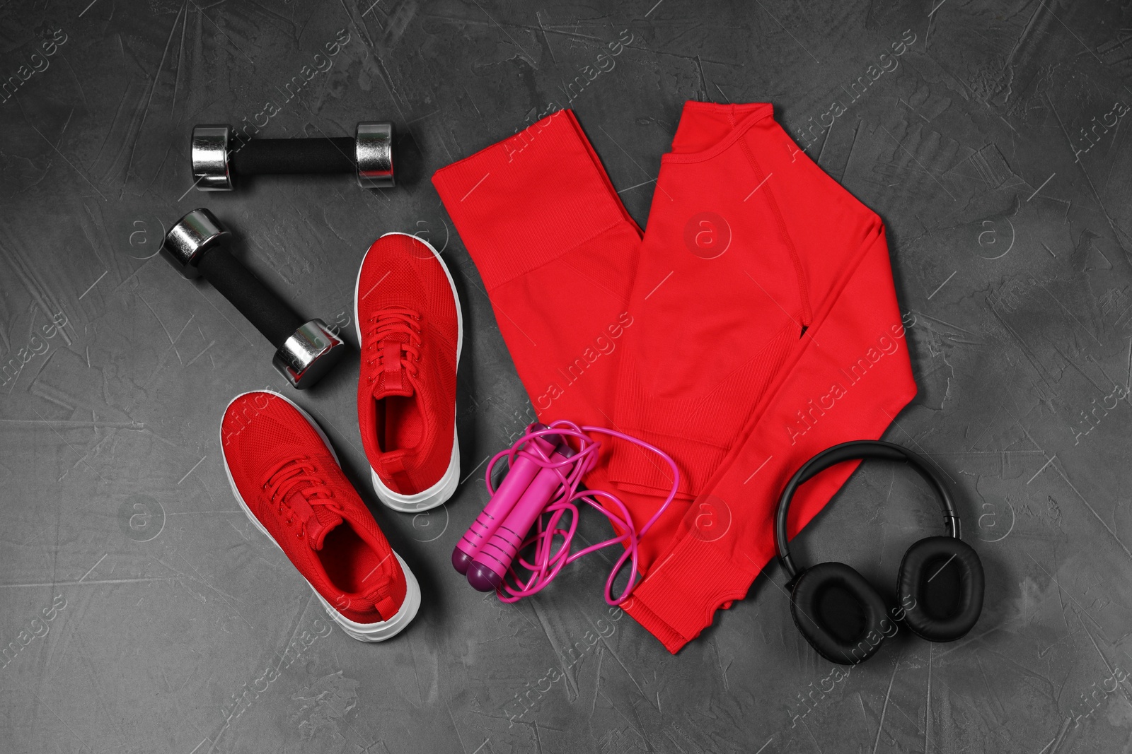 Photo of Stylish sportswear, dumbbells, red sneakers, skipping rope and headphones on grey background, flat lay