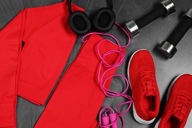 Photo of Stylish sportswear, dumbbells, red sneakers, skipping rope and headphones on grey background, flat lay