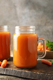 Photo of Fresh carrot juice in mason jars and vegetables on wooden table against gray background