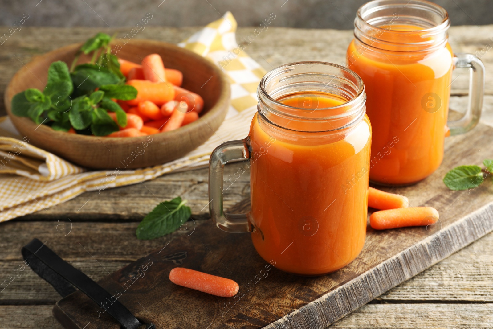 Photo of Fresh carrot juice in mason jars, vegetables and mint on wooden table