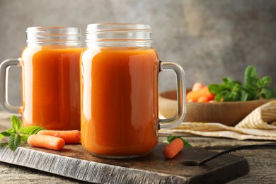 Photo of Fresh carrot juice in mason jars, vegetables and mint on wooden table against gray background