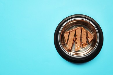 Photo of Wet pet food in feeding bowl on light blue background, top view. Space for text