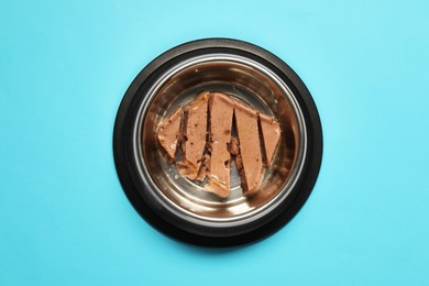 Photo of Wet pet food in feeding bowl on light blue background, top view