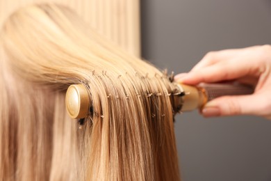 Photo of Hairdresser styling client's hair with round brush in salon, closeup