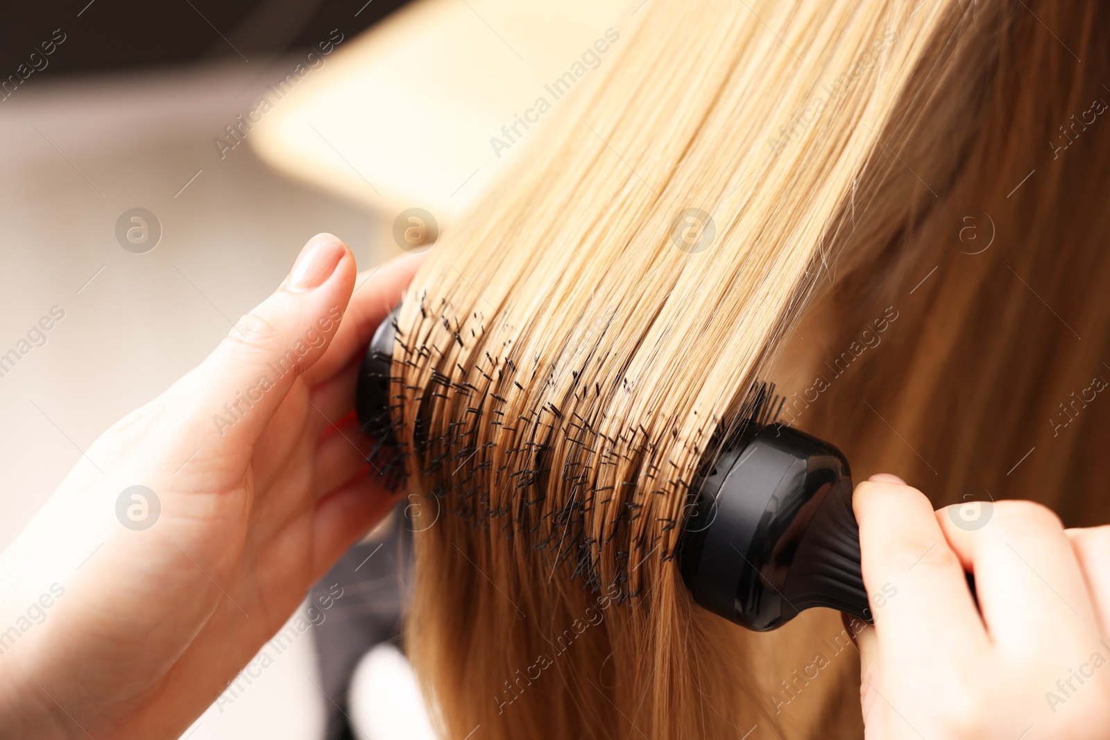 Photo of Hairdresser styling client's hair with round brush in salon, closeup