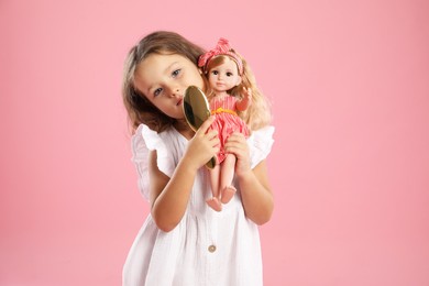 Photo of Cute little girl with doll and brush on pink background