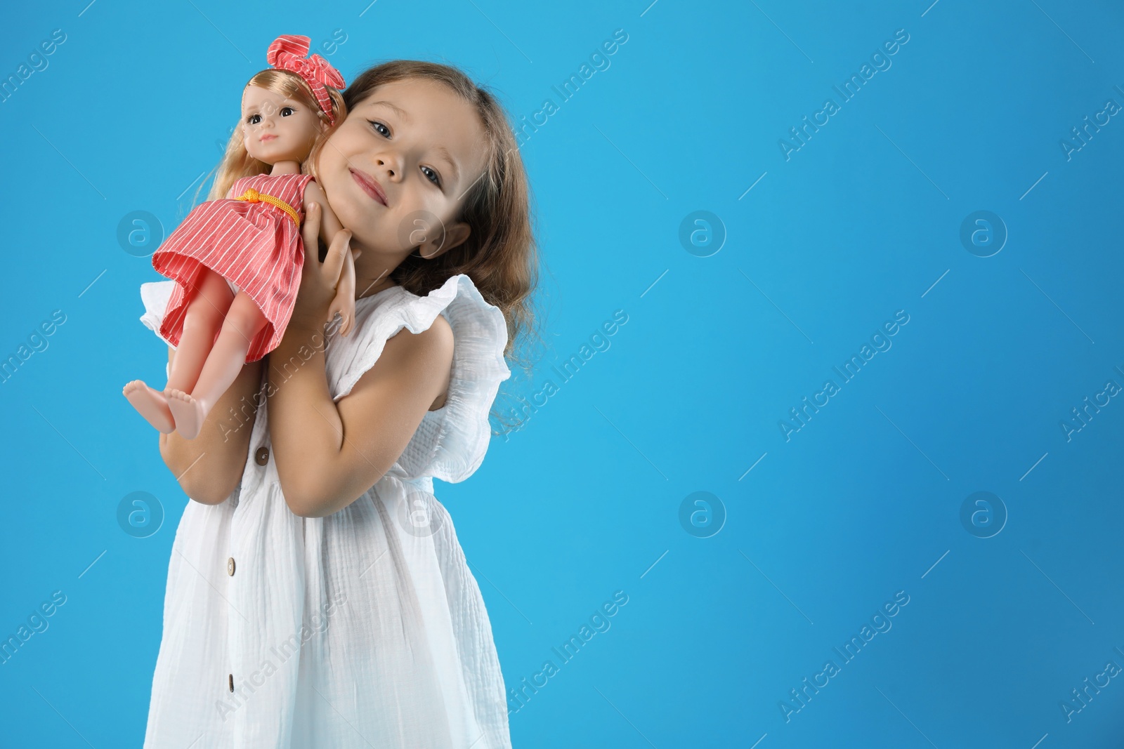 Photo of Cute little girl with doll on light blue background. Space for text