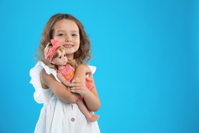 Photo of Cute little girl with doll on light blue background. Space for text