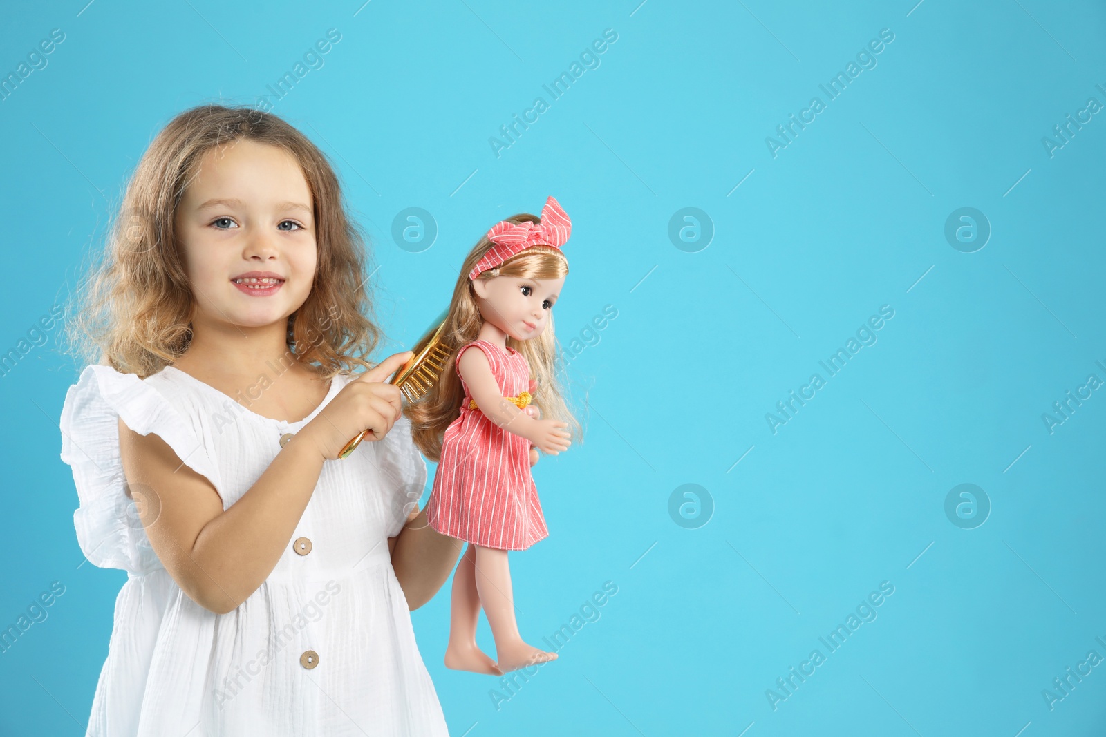 Photo of Cute little girl brushing doll's hair on light blue background. Space for text