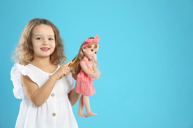 Photo of Cute little girl brushing doll's hair on light blue background. Space for text