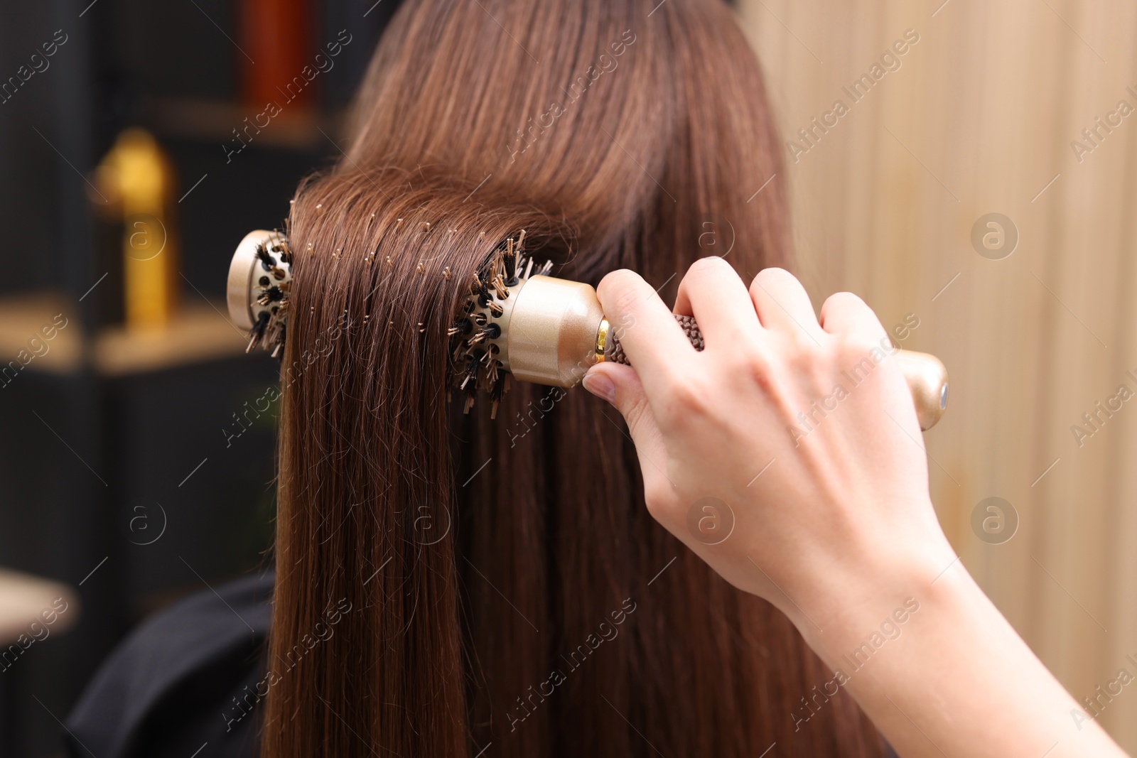 Photo of Hairdresser styling client's hair with round brush in salon, closeup