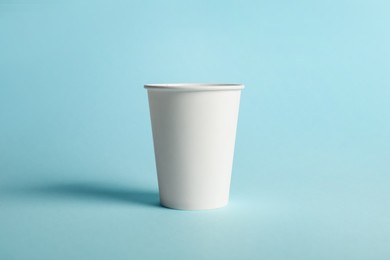 Photo of One paper cup on light blue background. Mockup for design