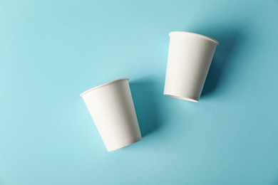Photo of Paper cups on light blue background, flat lay. Mockup for design