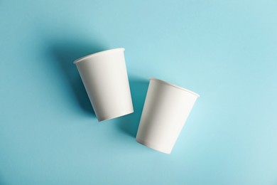 Photo of Paper cups on light blue background, flat lay. Mockup for design