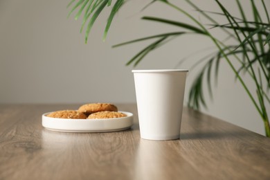 Photo of Paper cup and plate of cookies on wooden table in cafe. Mockup for design
