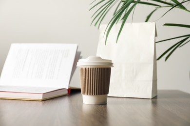 Photo of Paper cup, takeaway bag and book on wooden table indoors. Mockup for design