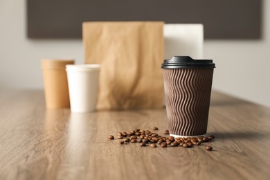 Photo of Paper cup and coffee beans on wooden table indoors. Mockup for design