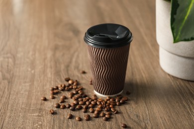 Photo of Paper cup and coffee beans on wooden table, closeup. Mockup for design