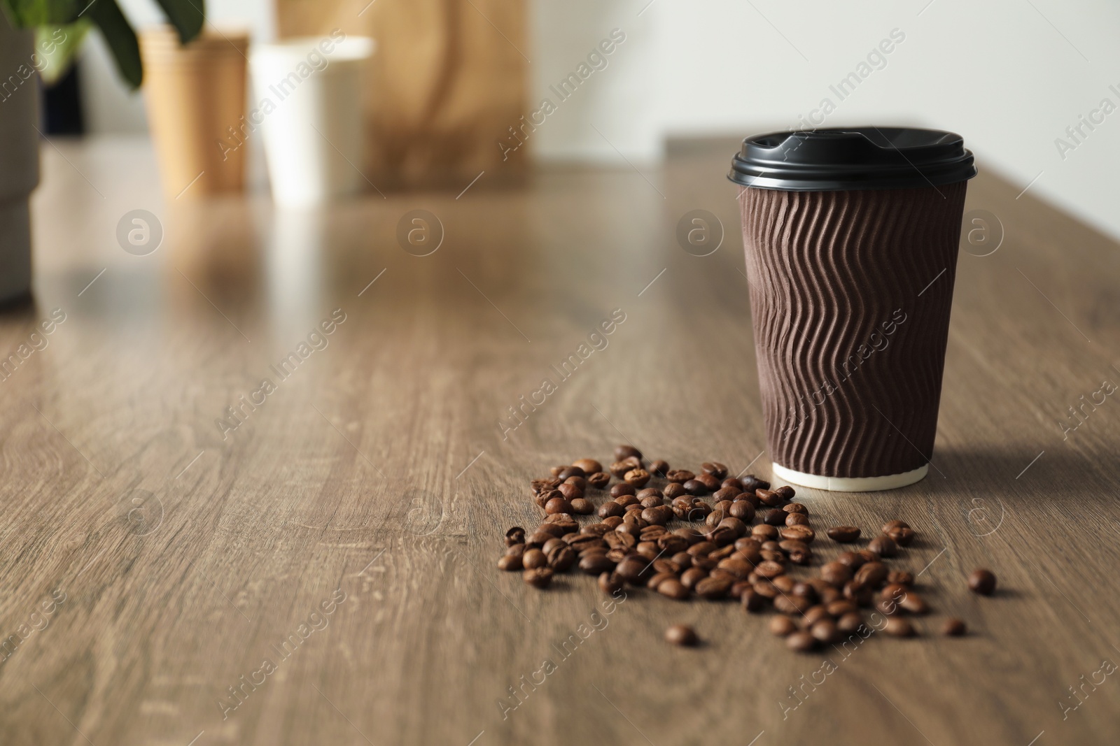 Paper cup and coffee beans on wooden table indoors. Mockup for design Photo of Paper cup and coffee beans on wooden table indoors. Mockup for design