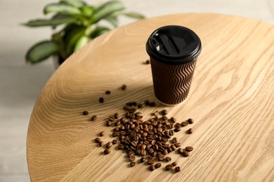 Photo of Paper cup and coffee beans on wooden table indoors. Mockup for design