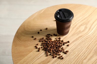 Photo of Paper cup and coffee beans on wooden table indoors. Mockup for design