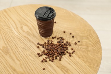Photo of Paper cup and coffee beans on wooden table indoors. Mockup for design