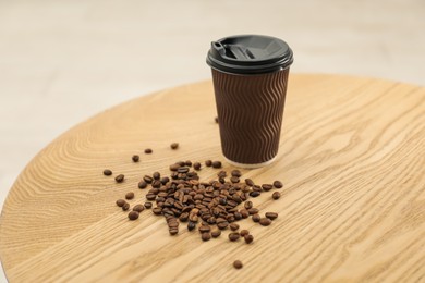 Photo of Paper cup and coffee beans on wooden table indoors. Mockup for design