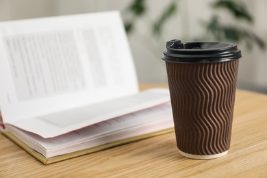 Photo of Paper cup and open book on wooden table indoors, closeup. Mockup for design