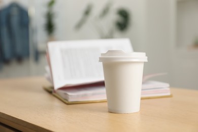Photo of Paper cup and open book on wooden table indoors, closeup. Mockup for design