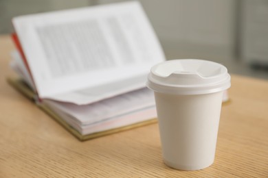 Photo of Paper cup and open book on wooden table indoors, closeup. Mockup for design