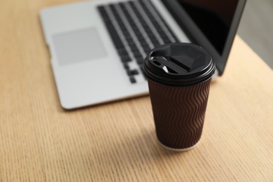 Photo of Paper cup and laptop on wooden table, closeup. Mockup for design