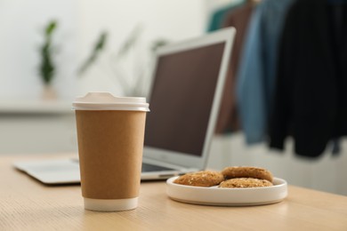 Photo of Paper cup, plate with cookies and laptop on wooden table indoors, closeup. Mockup for design