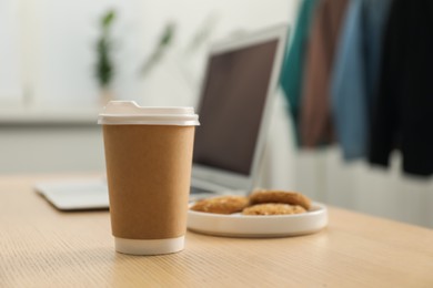 Photo of Paper cup, plate with cookies and laptop on wooden table indoors, closeup. Mockup for design