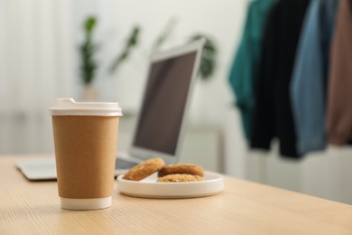 Photo of Paper cup, plate with cookies and laptop on wooden table indoors, closeup. Mockup for design
