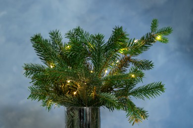 Photo of Beautiful fir tree branches decorated with Christmas lights on blue background, closeup