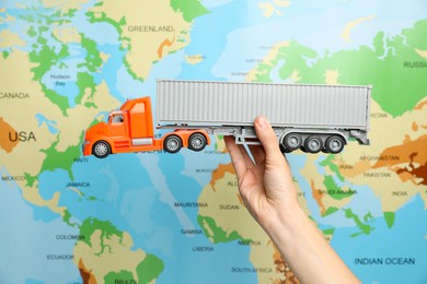 Photo of Woman with toy truck against world map, closeup. Logistics concept