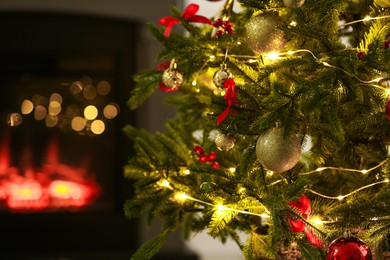 Photo of Beautiful decorated Christmas tree near fireplace at home, closeup. Bokeh effect