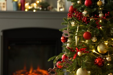 Photo of Beautiful decorated Christmas tree near fireplace at home, closeup. Space for text