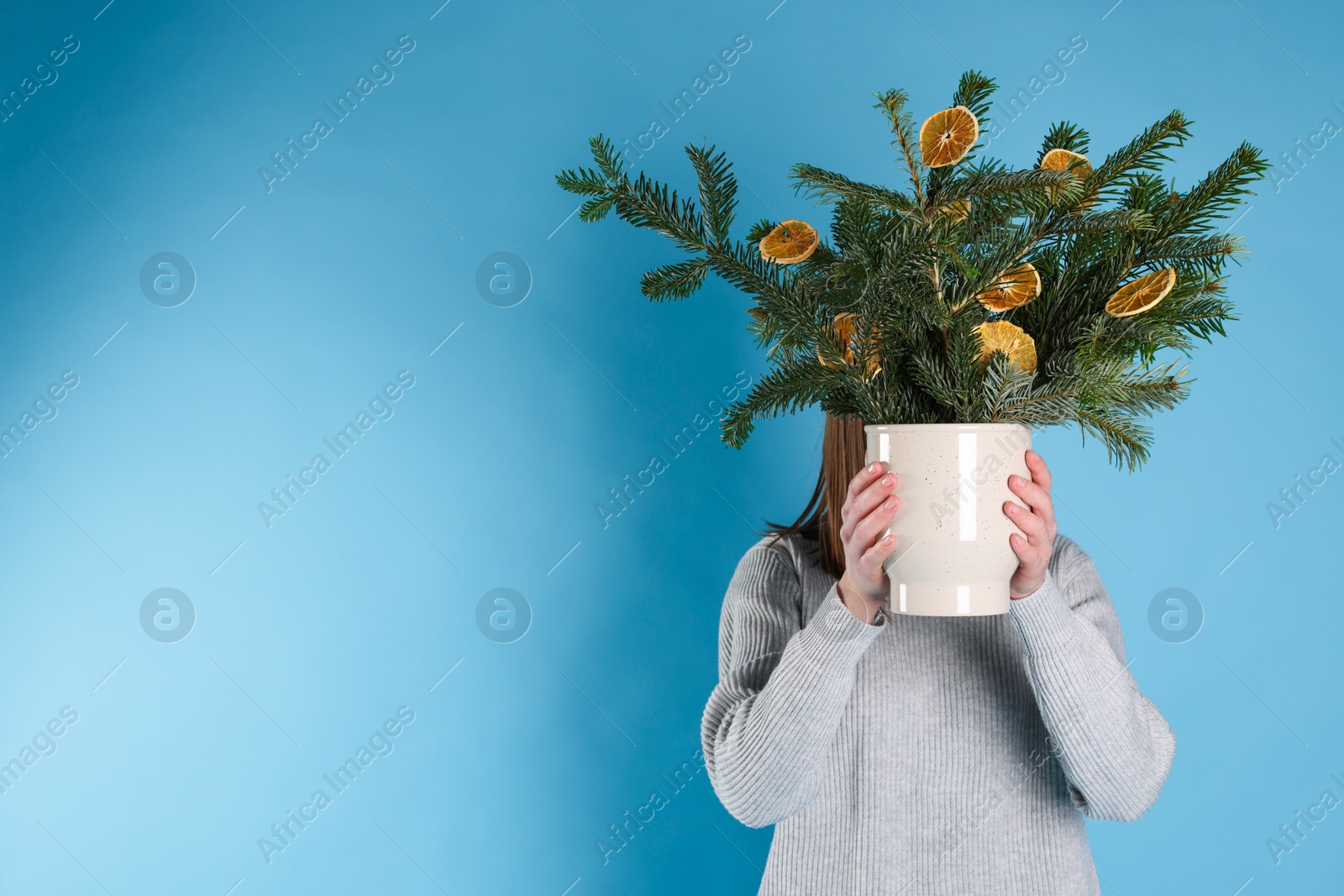 Photo of Woman holding beautiful Christmas composition of fir tree branches decorated with dried orange slices on blue background. Space for text